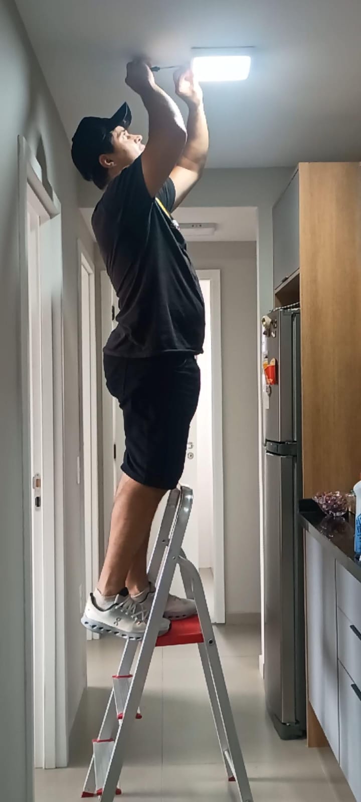 Profissional da JS Faz Tudo instalando uma luminária no teto do corredor de um apartamento